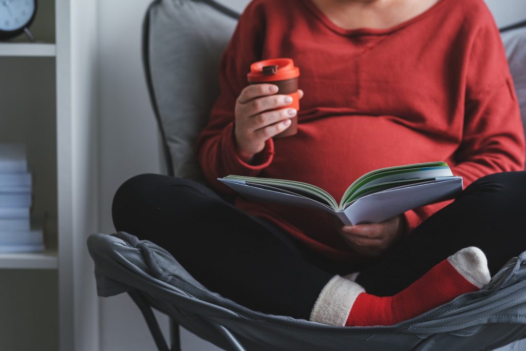 Pregnant woman sitting on chair relaxing and reading a book